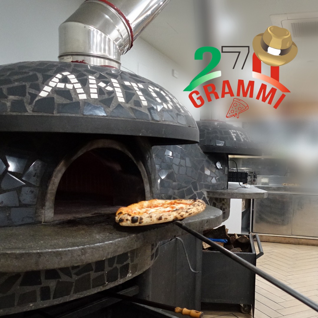 Pizza appena sfornata sulla pala davanti al forno a legna con cupola in mosaico nero, logo 270 Grammi